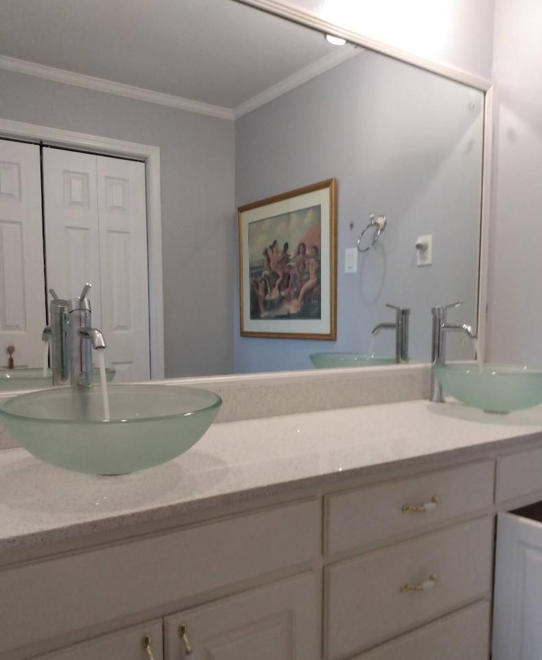 Bathroom with two sinks, a large mirror, white cabinets, and artwork on the wall.