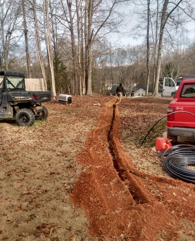 Trench dug in yard, person walking, UTV, red truck, trees, and landscape.