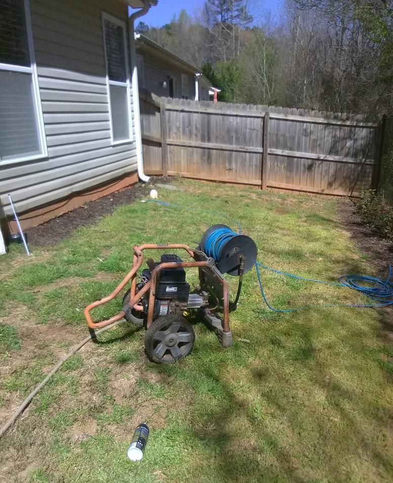 Pressure washer on a grassy lawn next to a house and a wooden fence.