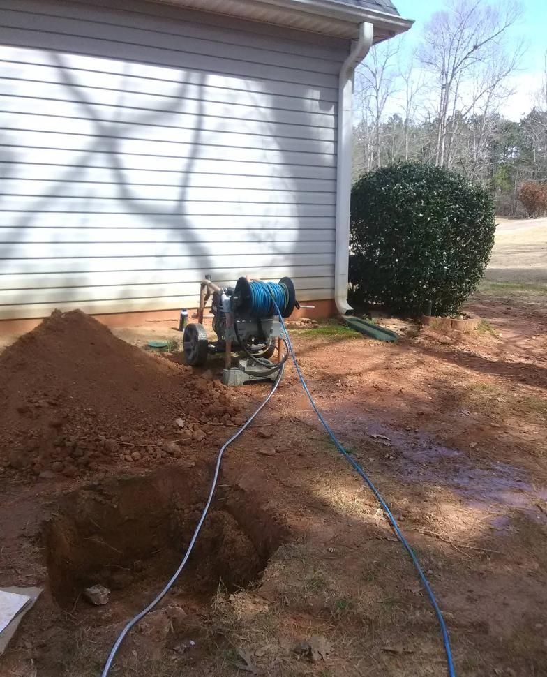 Hole dug in yard next to a house, with dirt pile and machine.