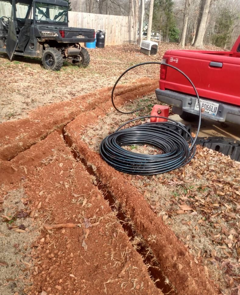 Trenches dug in red dirt with black tubing, red truck, and ATV in the background.
