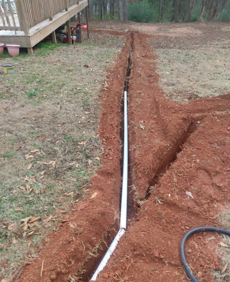 A white pipe in a trench of red soil, near a wooden deck.