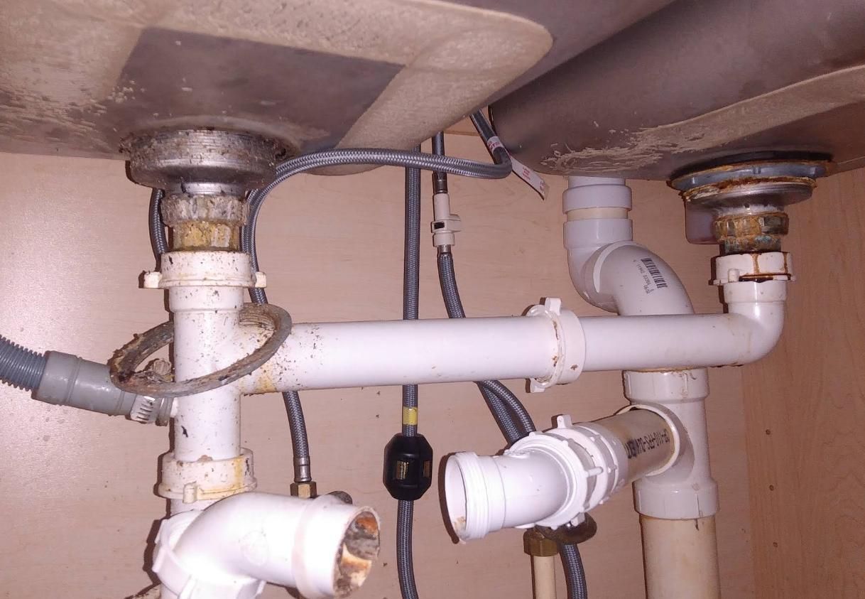 Plumbing under a double kitchen sink. White pipes connect drains. 