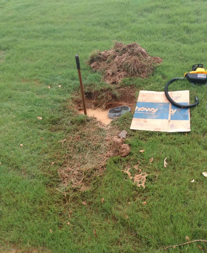 Hole dug in grass with dirt pile, shovel, and power tool.