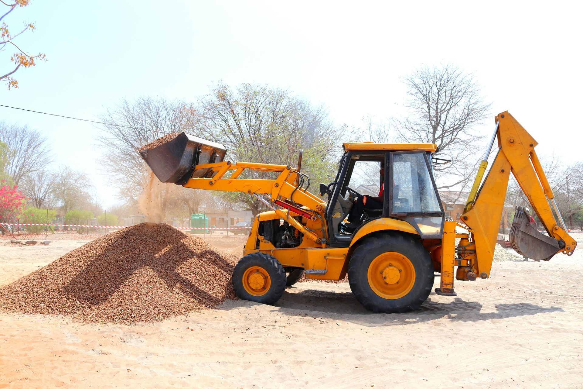 Yellow backhoe loading dirt onto a pile outdoors.