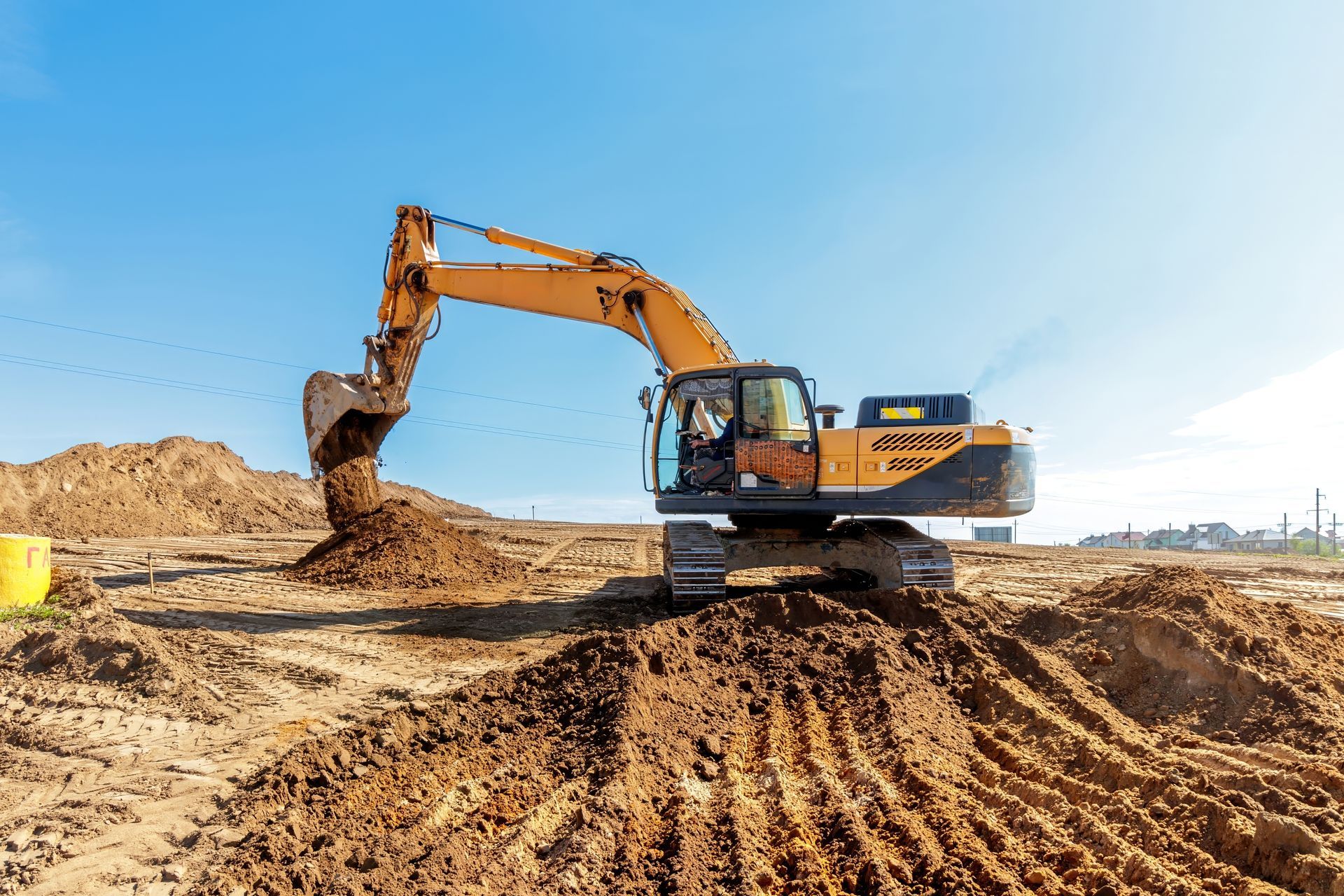 Yellow excavator digging and moving dirt on a construction site under a blue sky.