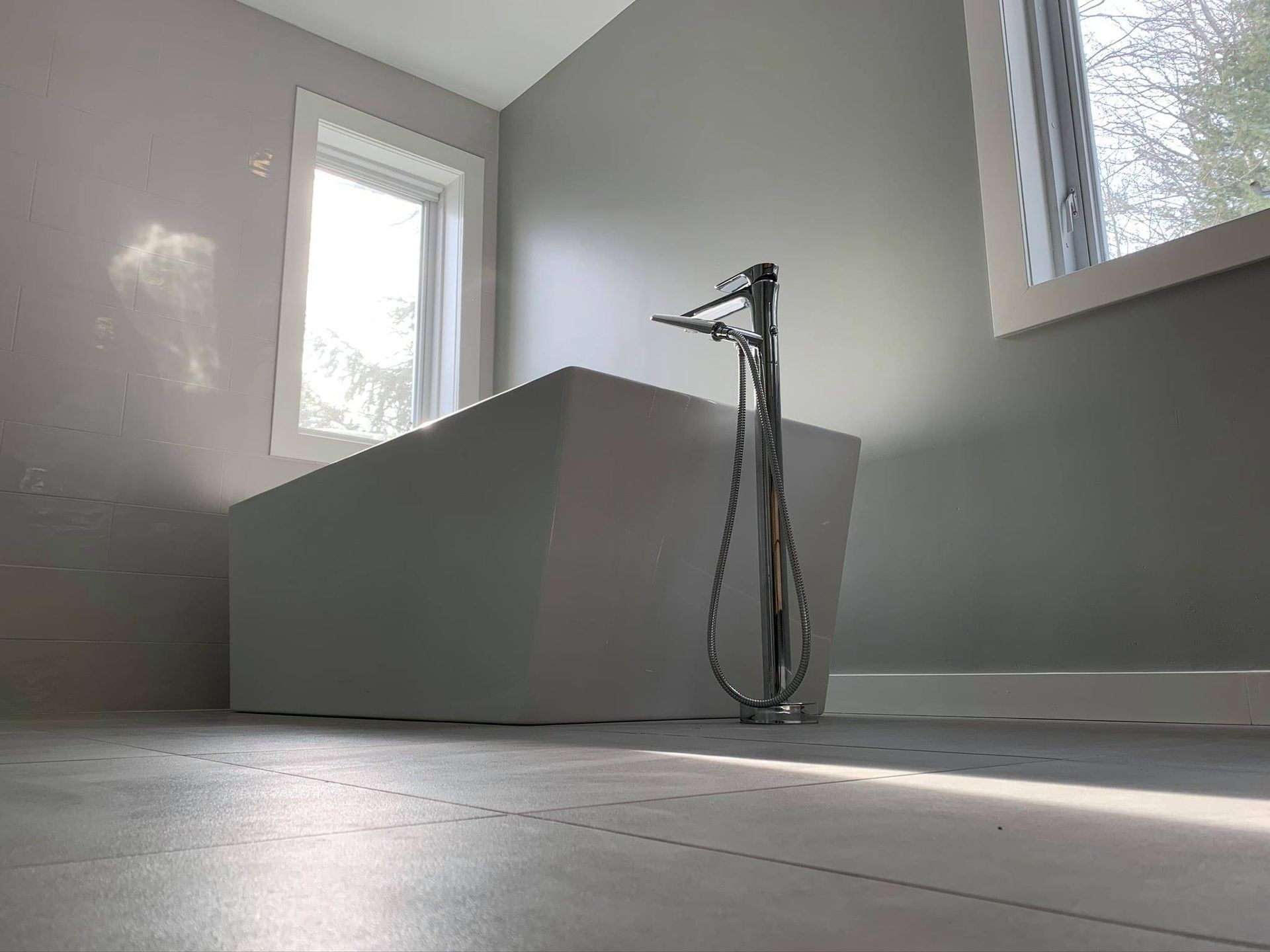 Salle de bains moderne avec baignoire îlot, robinet chromé et fenêtre laissant entrer la lumière naturelle.