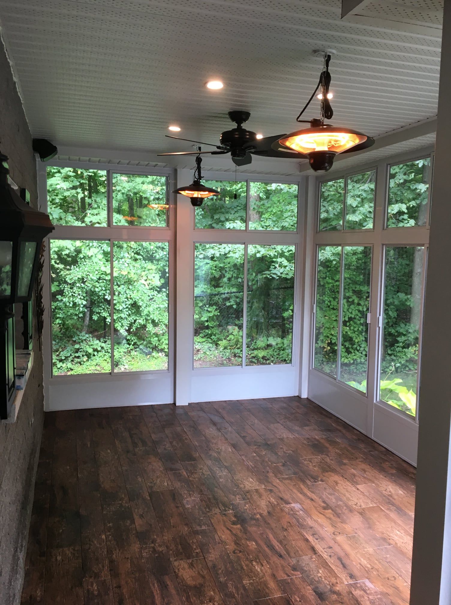 Véranda avec de grandes fenêtres, parquet, ventilateurs de plafond et vue sur l'extérieur.