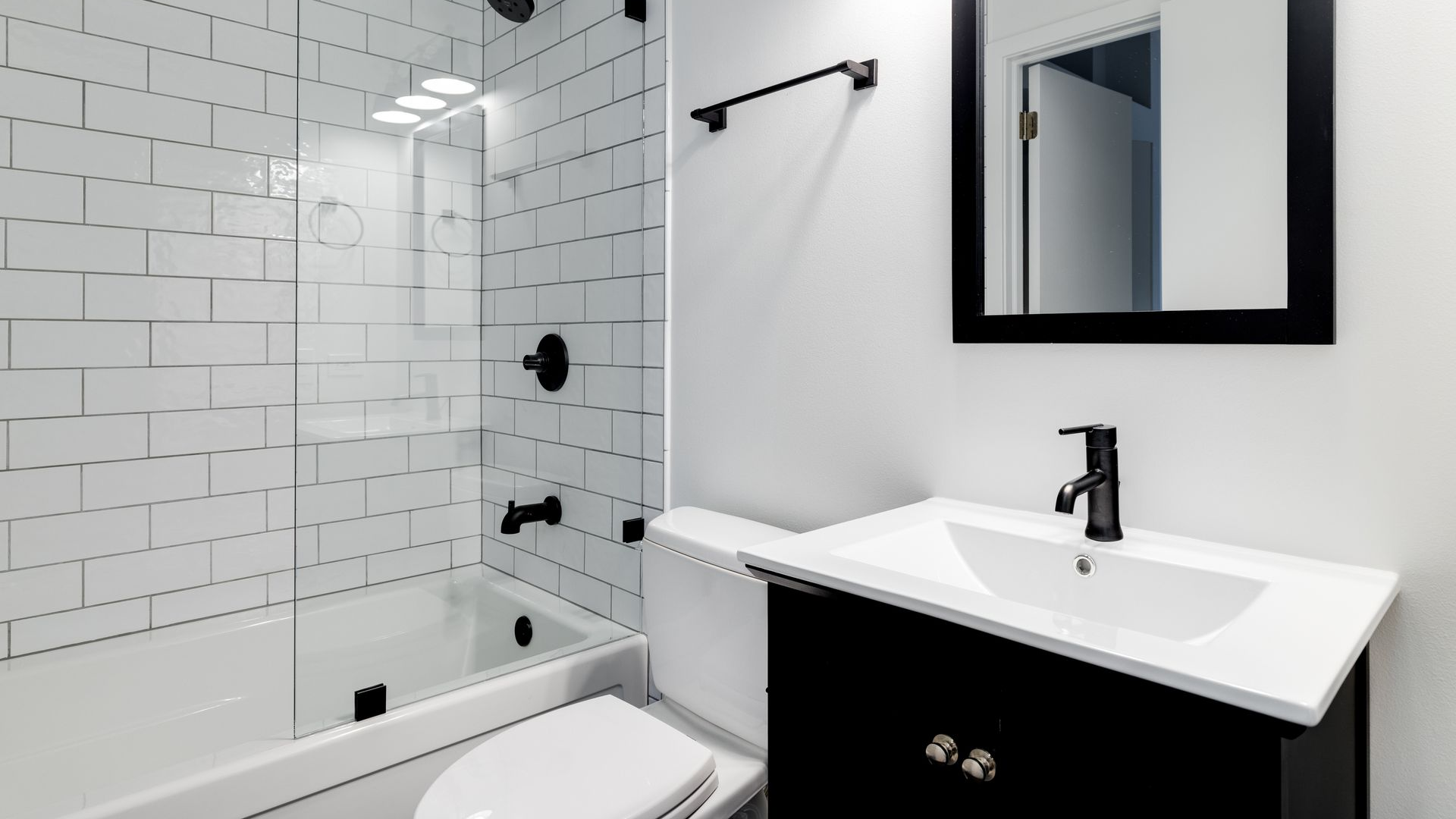 Salle de bains moderne blanche avec des touches de noir : douche, meuble-lavabo, toilettes et miroir.