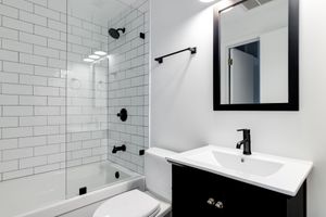 Salle de bains moderne blanche avec douche carrelée de carrelage métro, robinetterie noire et meuble-lavabo noir.