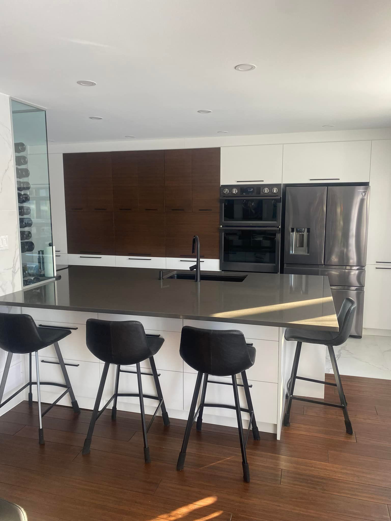 Cuisine moderne avec îlot central, coin repas, appareils électroménagers foncés et mur lambrissé.