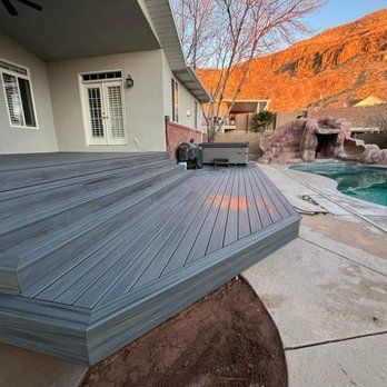 A gray composite deck extending from a house with a pool in the background. The setting is outdoors with a mountain backdrop.