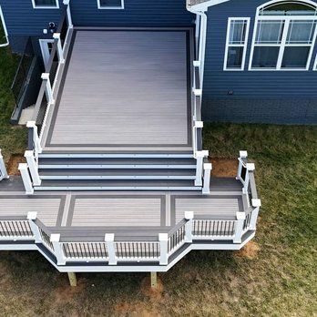 An elevated outdoor deck with gray and white composite boards, stairs, and railing on a house with blue siding.