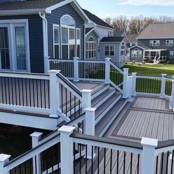 A multi-level gray composite deck with white posts and black railings attached to a blue house. Steps lead to a lower level.