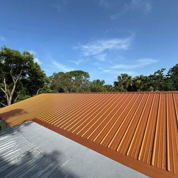 Orange corrugated metal roof against a blue sky with wispy clouds, trees in the background.