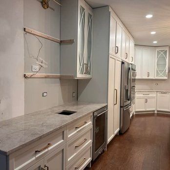 Kitchen renovation in progress, featuring white cabinets, gray countertops, a built-in wine cooler, and stainless steel appliances.