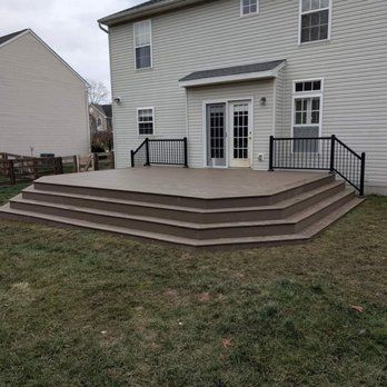 A multi-level composite deck with black railings extends from a two-story house into a grassy backyard.