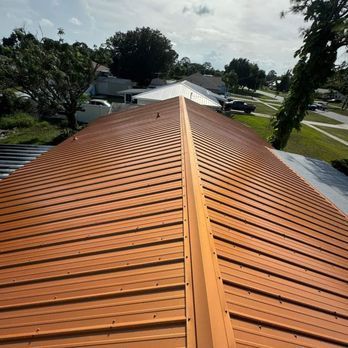 Copper-colored metal roof with ribbed design, viewed from above on a sunny day, in a suburban setting.