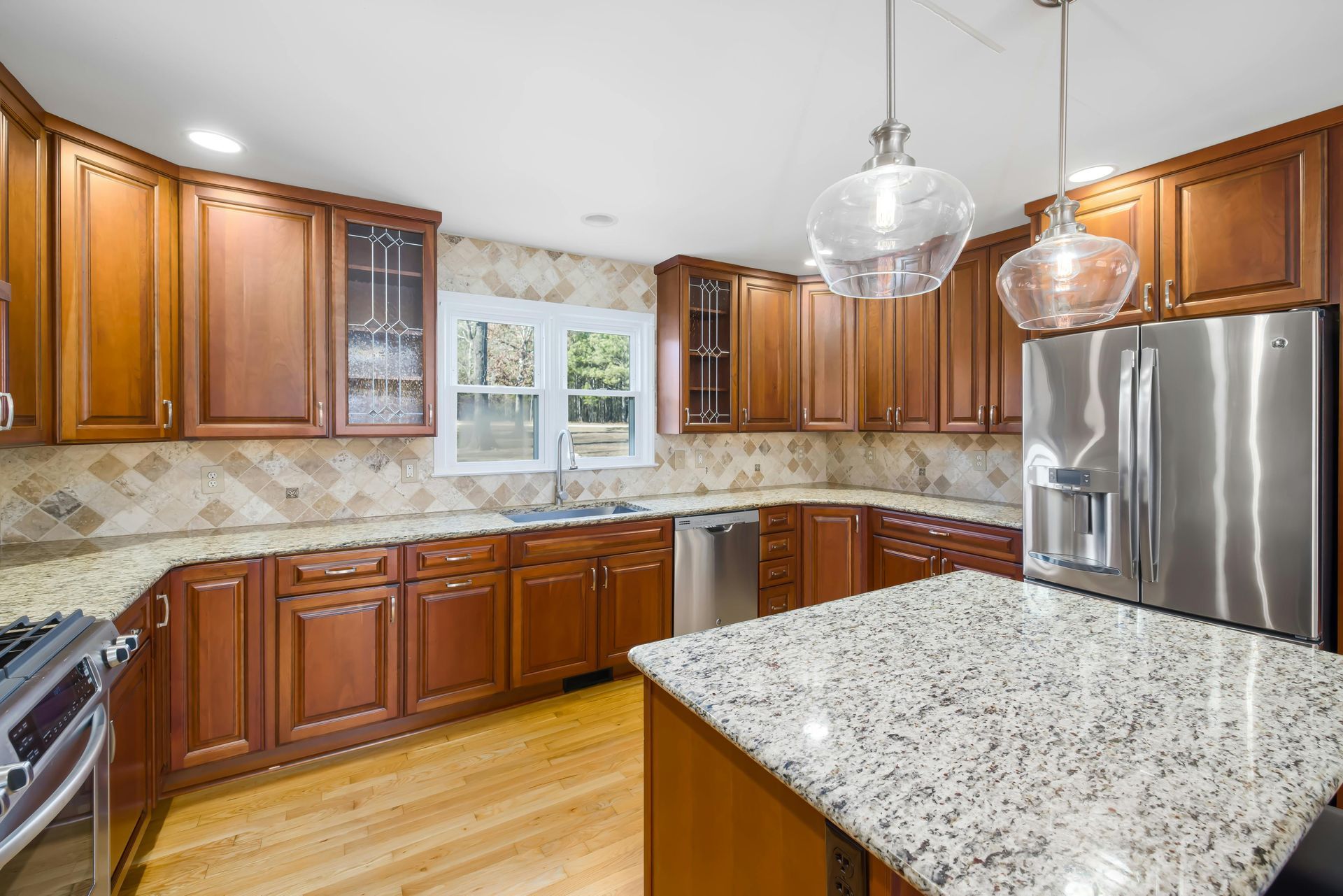 A kitchen with wood cabinets, granite countertops, and stainless steel appliances. Two pendant lights hang over an island.