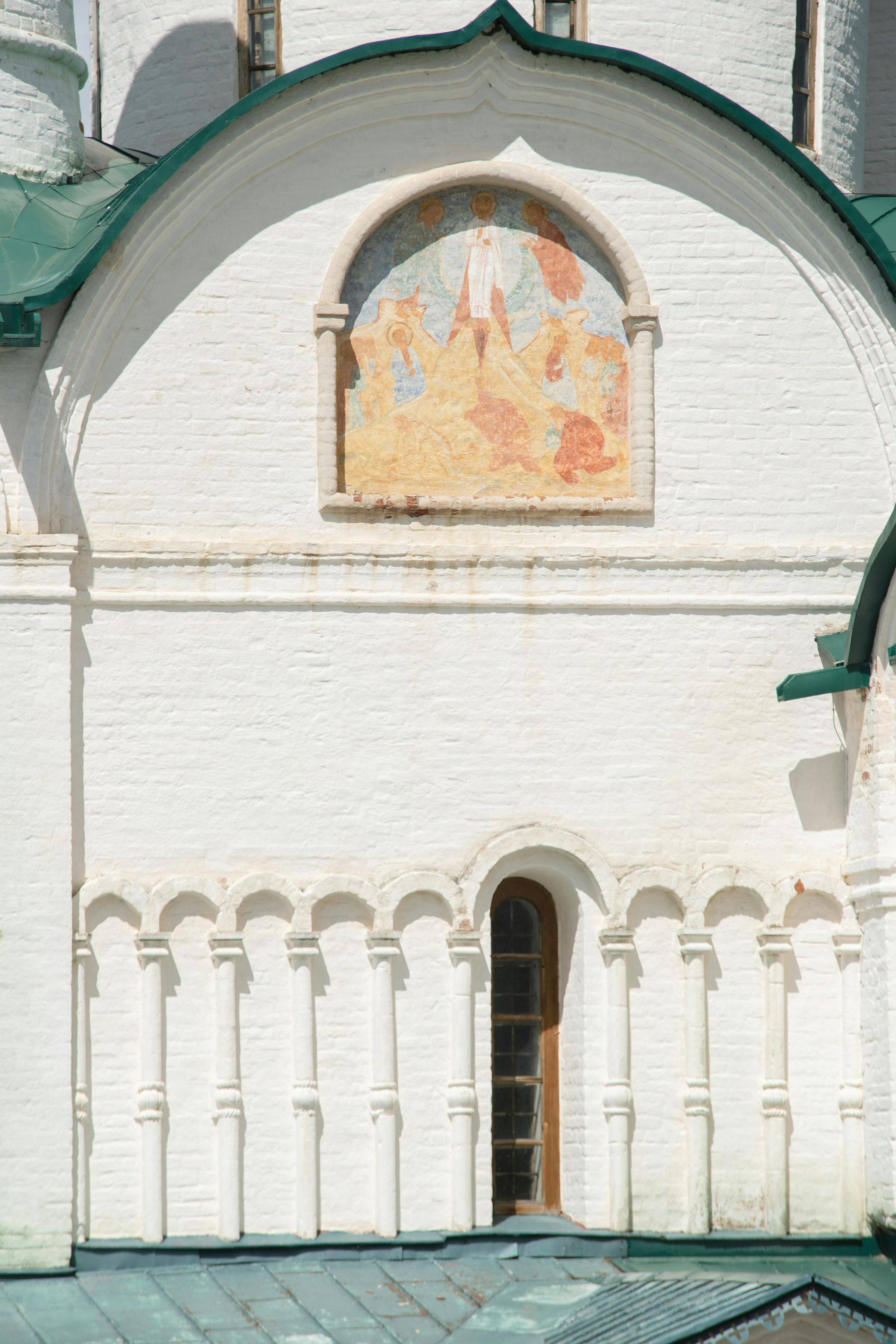 White brick building facade with a green roof, arched window, and faded mural.
