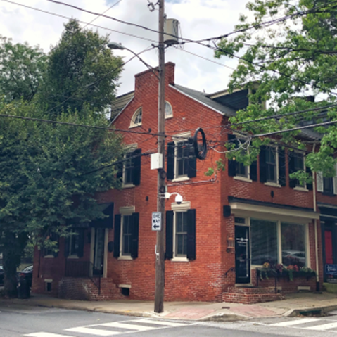 A red brick building with black shutters is on the corner of a street