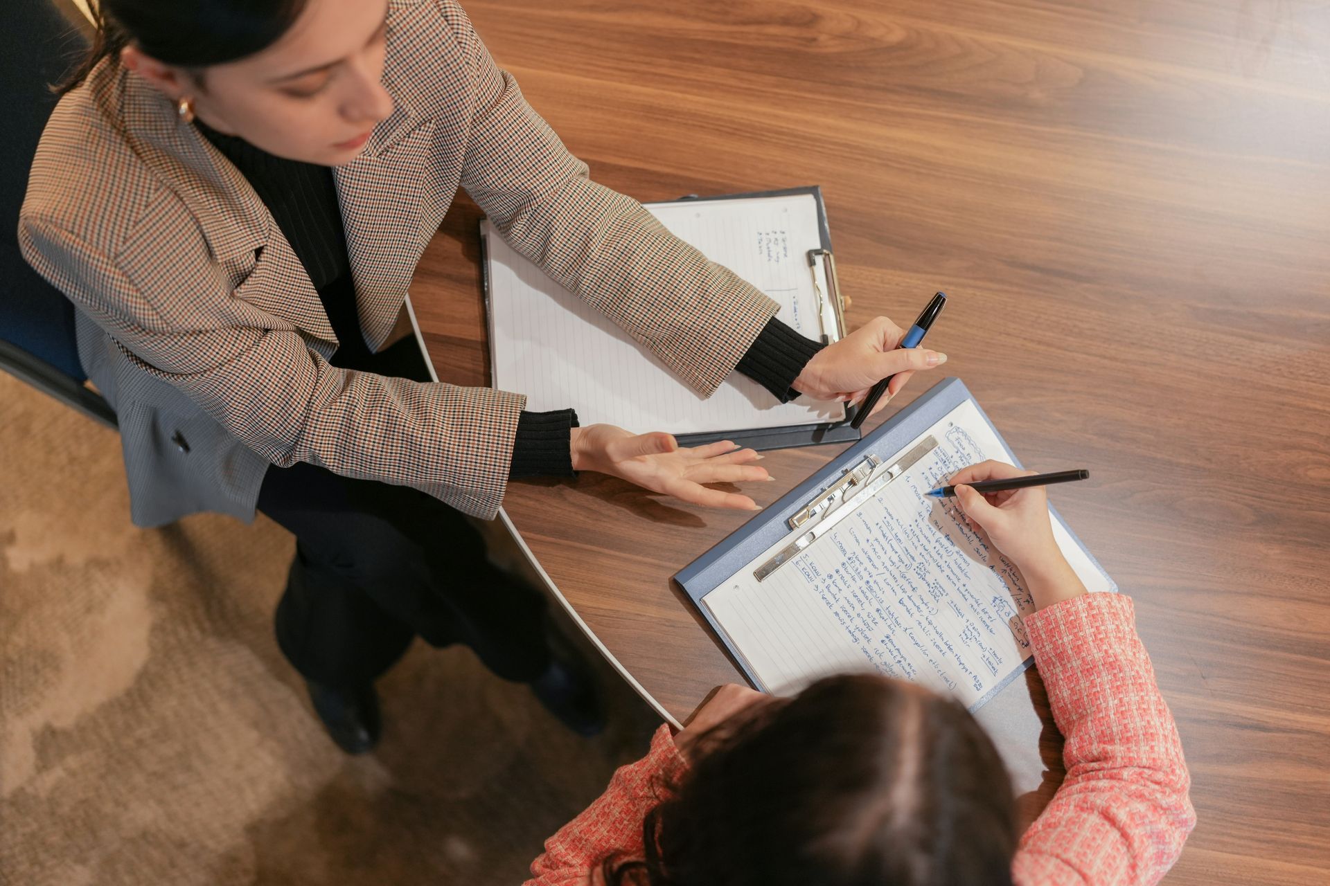 A woman is sitting at a table talking to another woman who is writing on a clipboard.