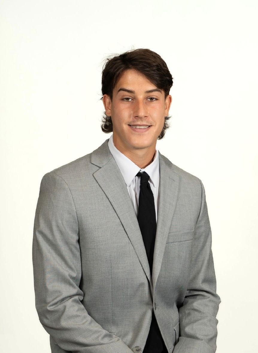 A man in a suit and white shirt is sitting on a stone wall.
