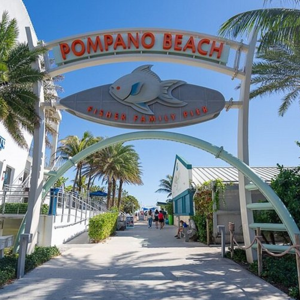 Entrance archway to Pompano Beach, Florida. Sign with fish logo, path to beach, palm trees.