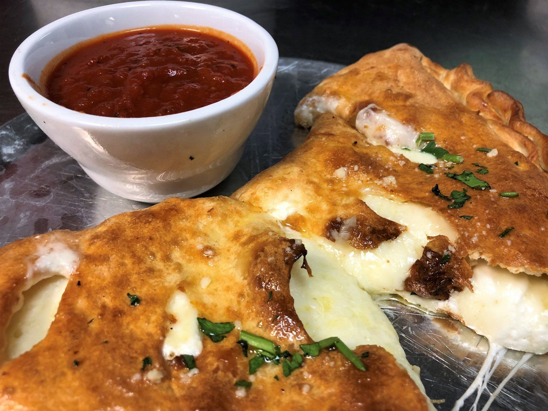 Calzone halves with cheese and meat, served with tomato sauce in a white bowl.