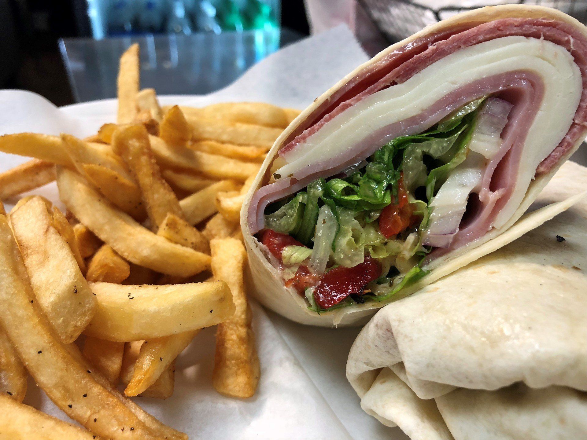 Wrap sandwich with fries. Sandwich has ham, cheese, lettuce, tomato. Fries are golden brown.