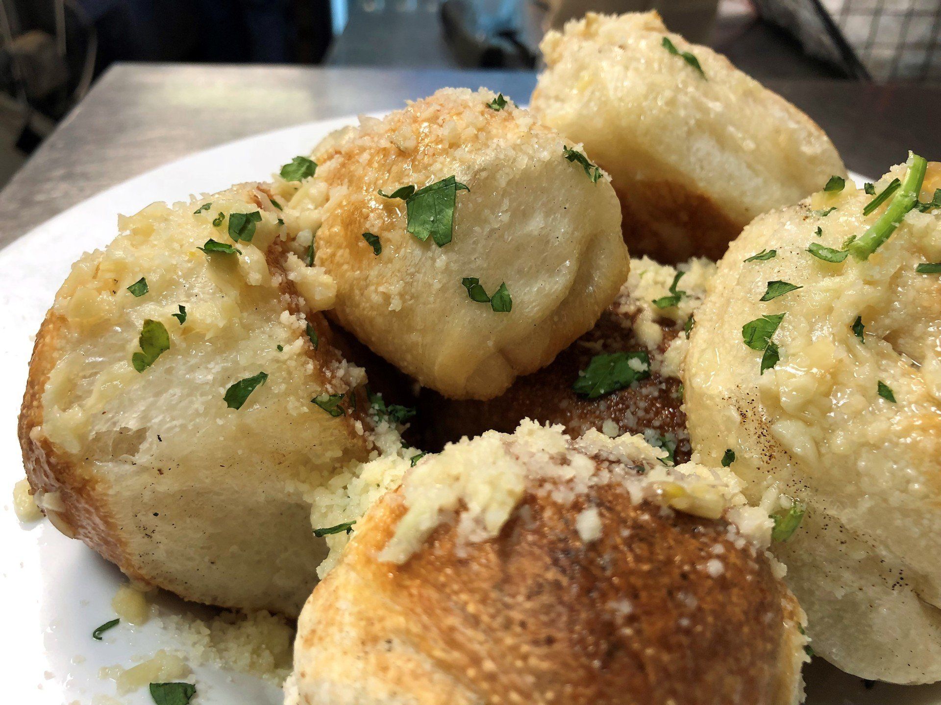Garlic knots, golden brown, topped with cheese and parsley, on a white plate.