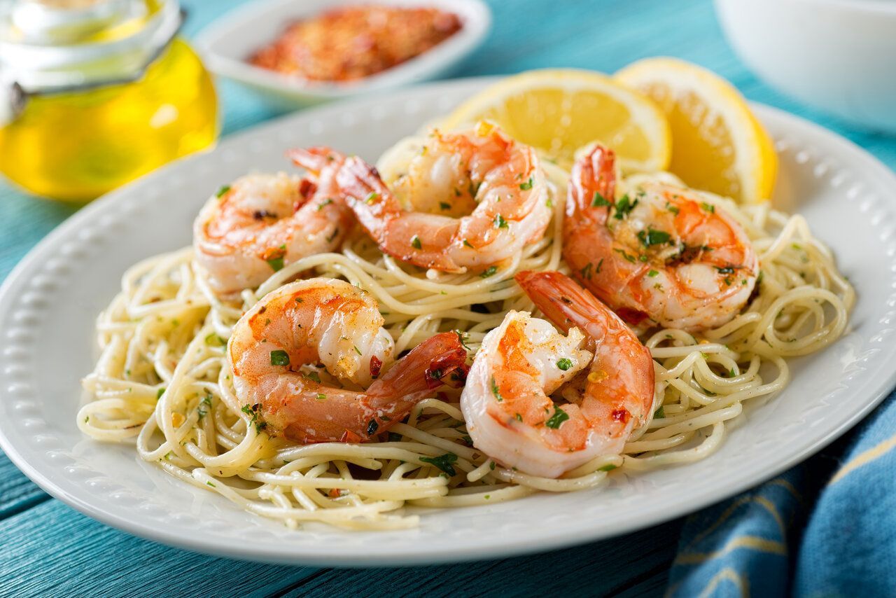 Shrimp scampi with pasta and lemon wedges on a white plate.