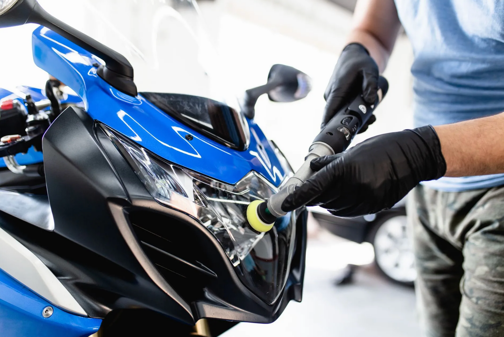 Person wearing black gloves polishing a blue and black motorcycle headlight.