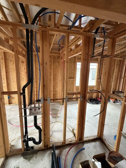 Unfinished house interior with exposed wood framing, floor joists, and plumbing pipes.