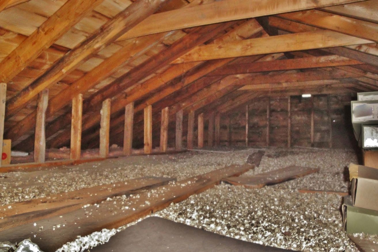 An attic space with exposed wooden rafters, light-colored insulation covering the floor, and some stored boxes.