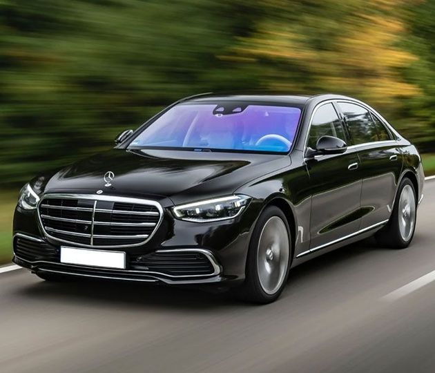 A black mercedes benz s class is driving down a road.