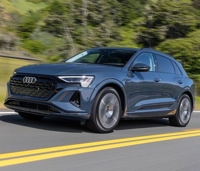 A blue audi e-tron is driving down a road.