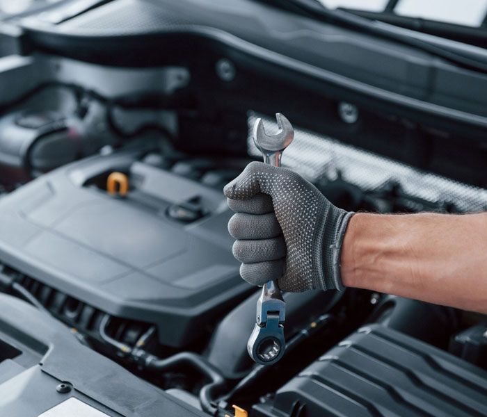 A person is holding a wrench in front of a car engine