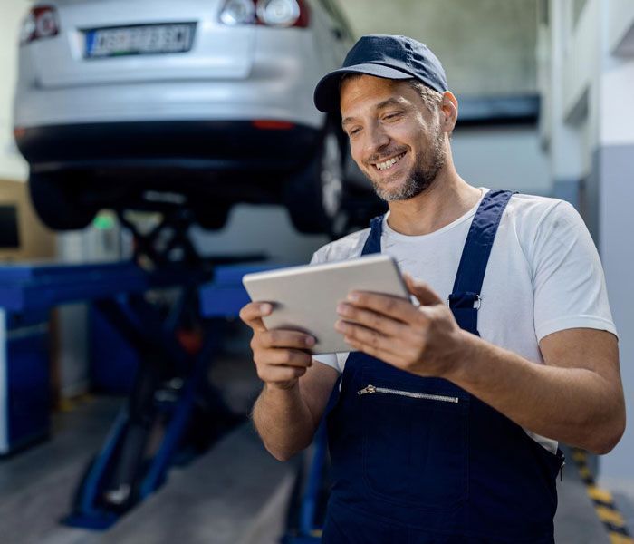 A man is using a tablet in a garage in front of a car.