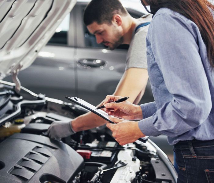 A man and a woman are looking under the hood of a car