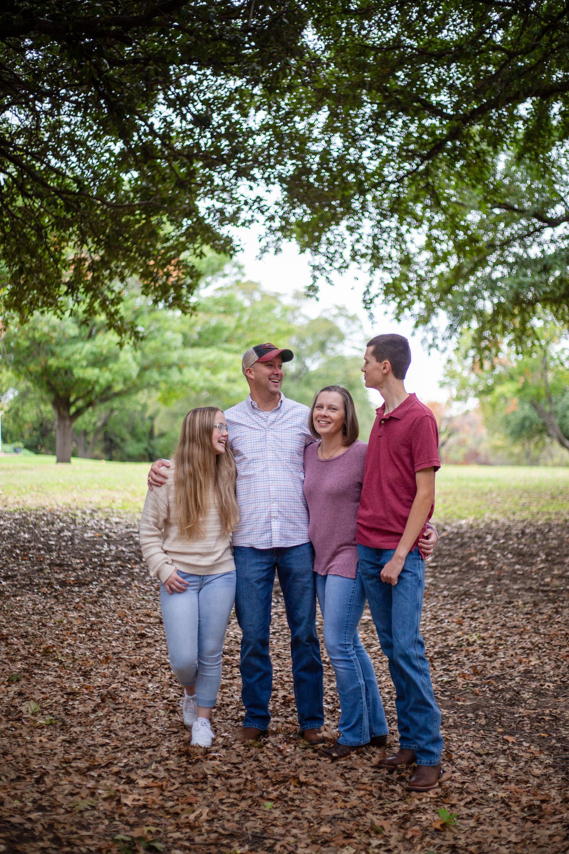 A family is standing under a tree in a park. Family photos by Sarah Rosie Studios.