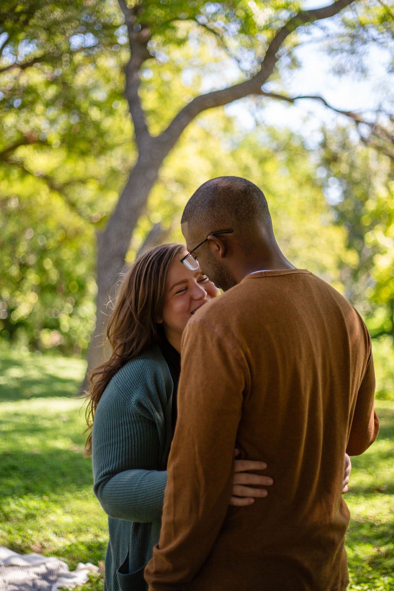 A man and a woman are hugging each other in a park. Couple photos by Sarah Rosie Studios.