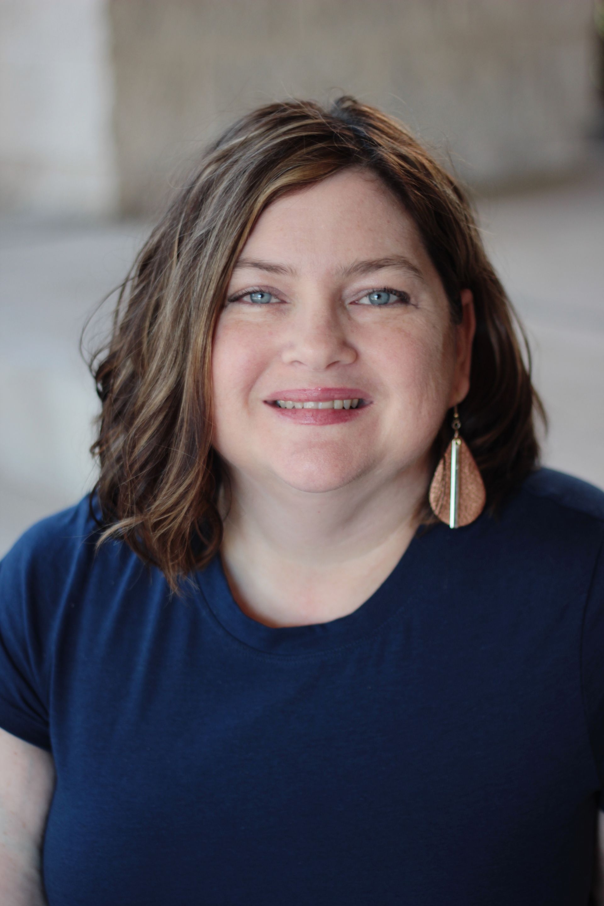A woman wearing a blue shirt and earrings is smiling for the camera. Corporate headshots by Sarah Rosie Studios.