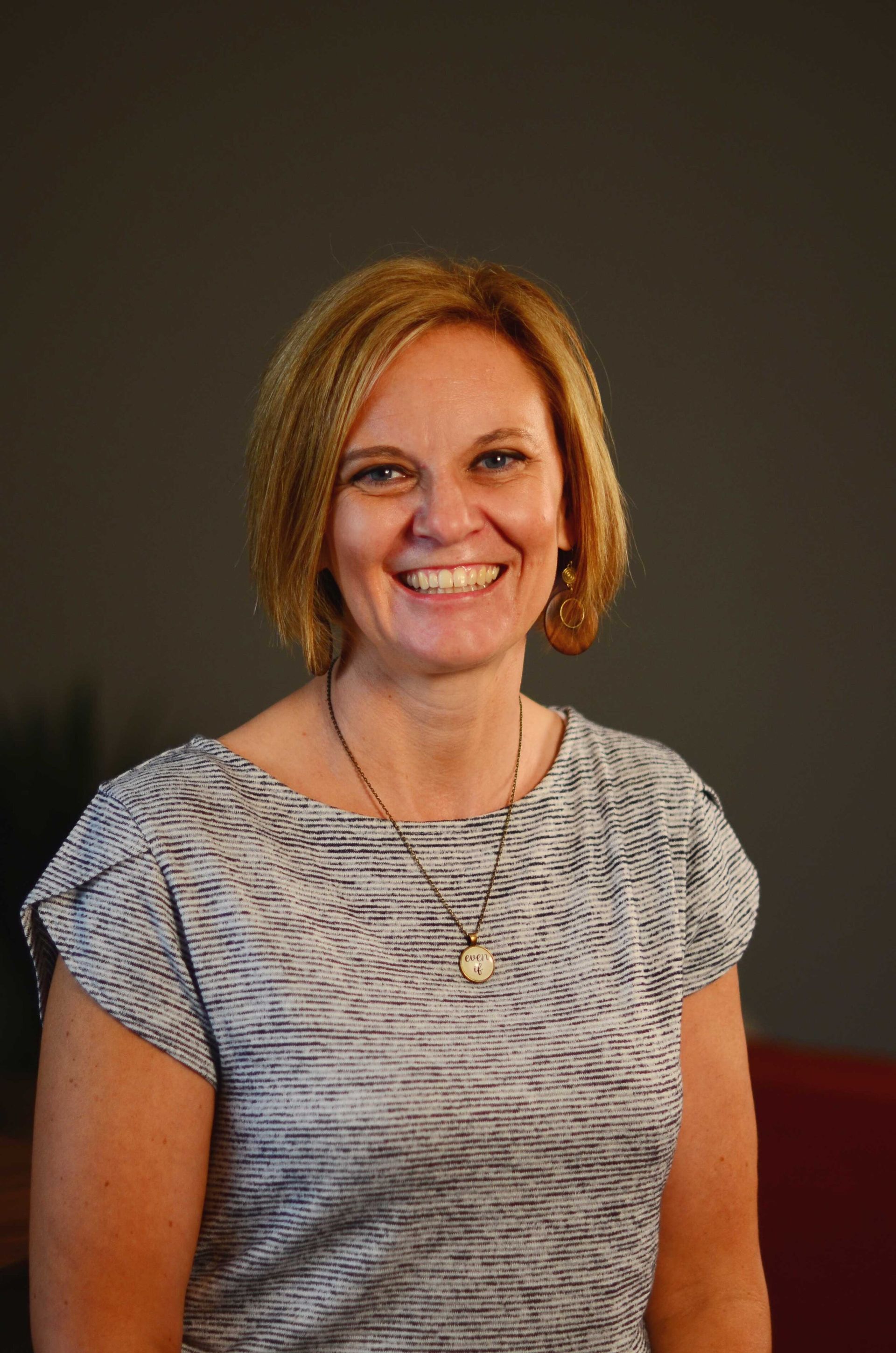 A woman wearing a gray shirt and a necklace is smiling for the camera. Corporate headshots by Sarah Rosie Studios.