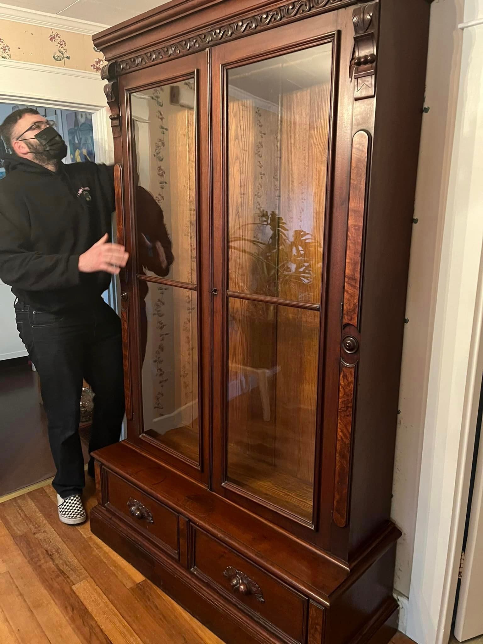 a man wearing a mask is standing next to a large wooden cabinet .