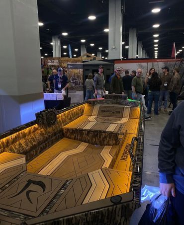 Indoor miniature golf course with a raised, illuminated track and people gathered around it at an expo.