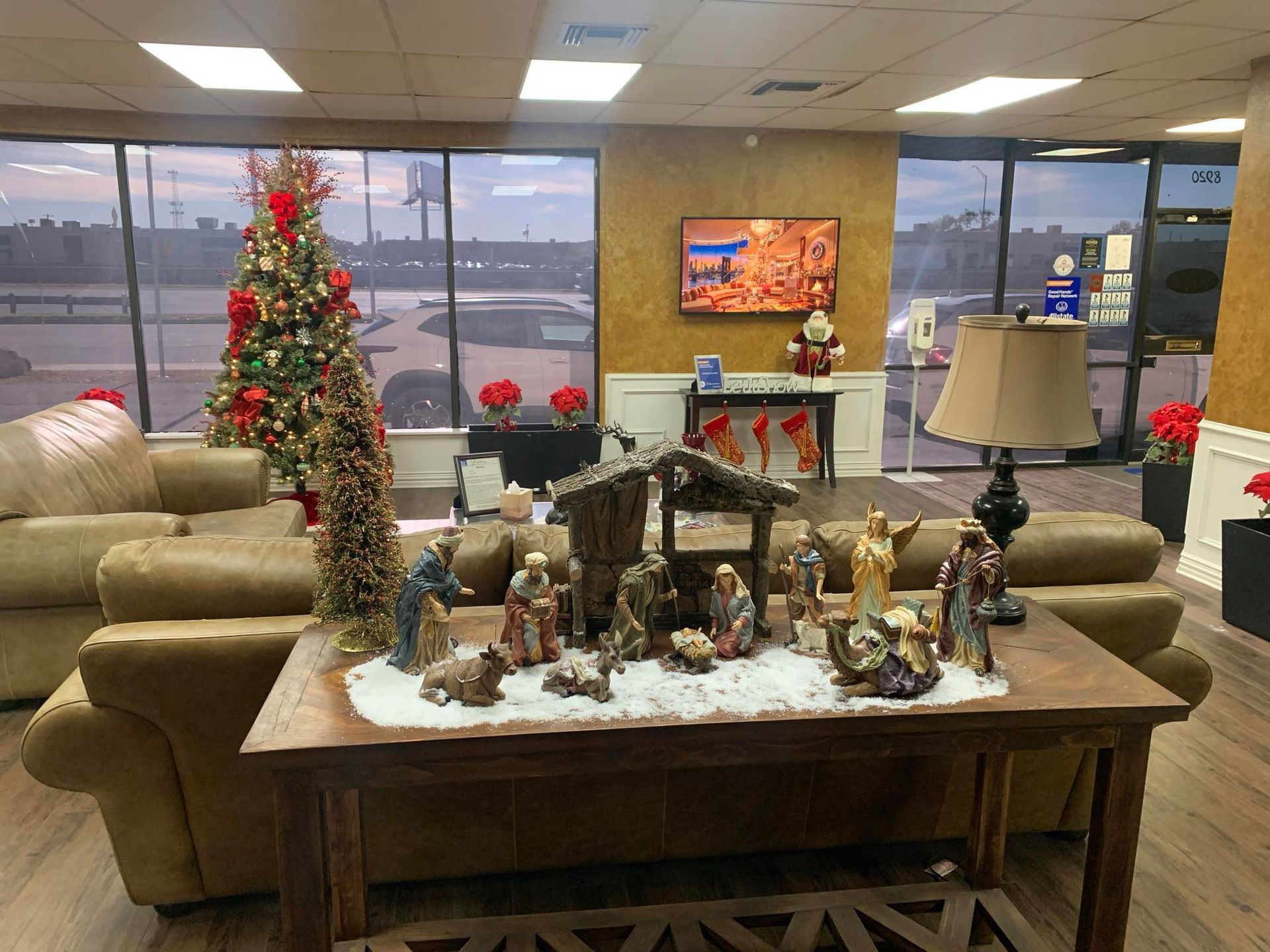 Christmas display: Nativity scene on a table, Christmas tree, sofa, and window with outdoor view.