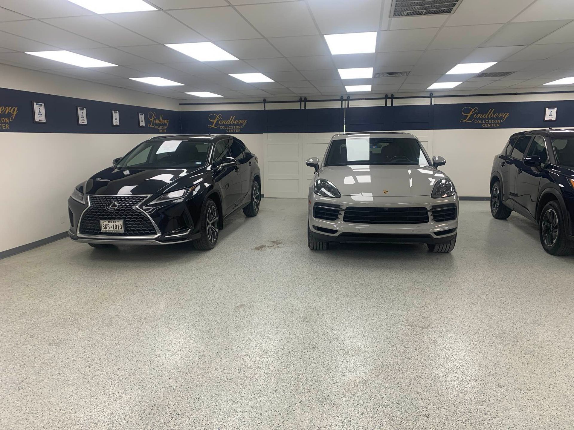 Three cars parked inside a dealership; a black Lexus, a silver SUV, and a black SUV.
