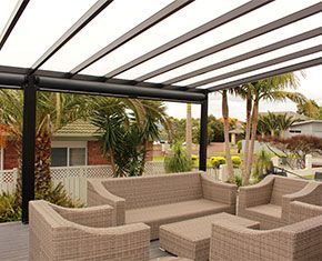 Patio with wicker furniture beneath a black-framed canopy. Palm trees and a house are visible in the background.