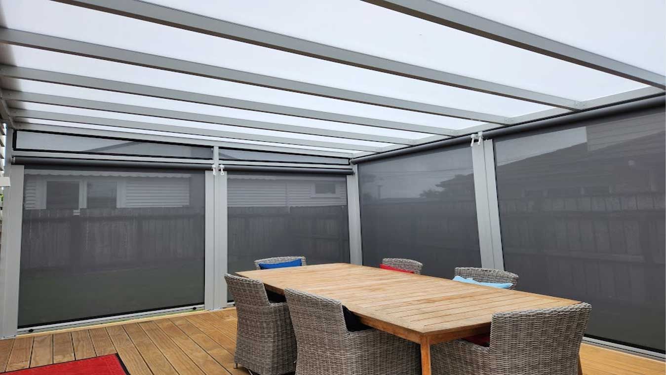 Outdoor dining area with a wooden table and chairs, under a pergola with shades.
